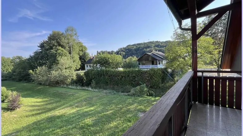 Überdachter Balkon mit Holzboden und weitem Blick ins Grüne und auf die umliegende Landschaft.