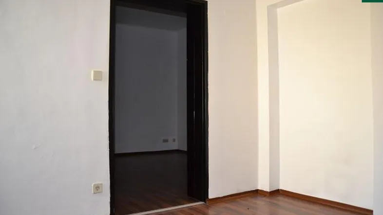 Leerer Raum mit dunklem Holzboden und Türrahmen, der zu einem weiteren Zimmer führt.