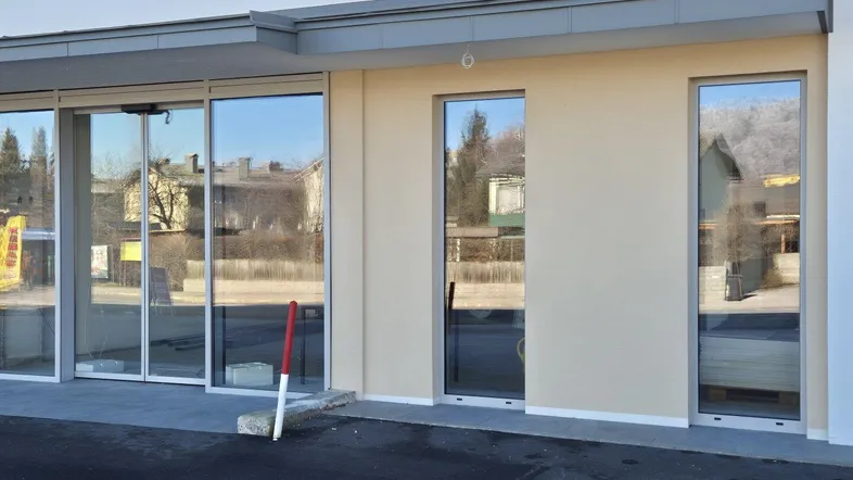Moderne Gebäudefassade mit großen Glasfronten und automatischen Schiebetüren, die eine helle und einladende Eingangspartie bilden.