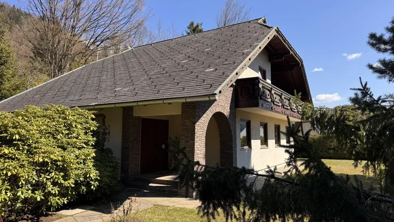 Traditionelles Einfamilienhaus mit Satteldach und Balkon, umgeben von einem gepflegten Garten an einem sonnigen Tag.