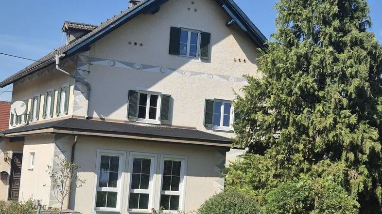 Traditionelles Haus mit beiger Fassade, grünen Fensterläden und Satteldach.