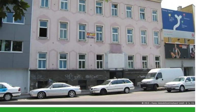 Historisches Mehrfamilienhaus mit beigefarbener Fassade und vielen Fenstern an einer belebten Straße.