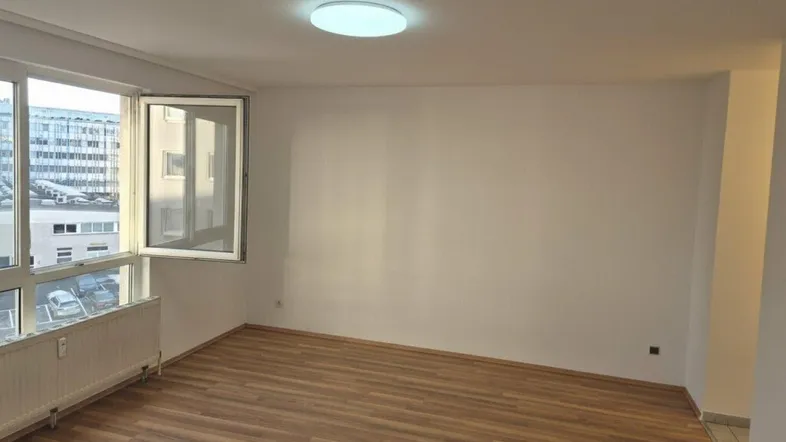 Helles, leeres Zimmer mit Laminatboden und großem Fenster, ideal als Wohnbereich nutzbar.