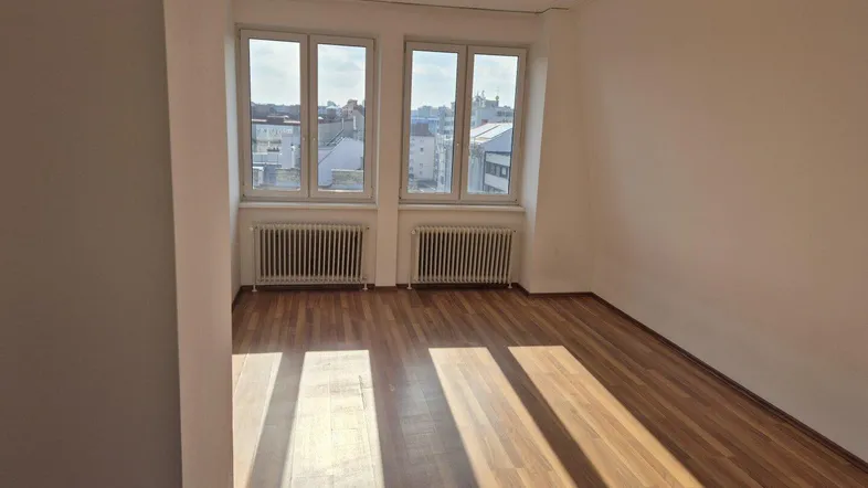 Helles Zimmer mit Holzfußboden und Blick auf die Stadt, ausgestattet mit Heizkörpern unter den Fenstern.