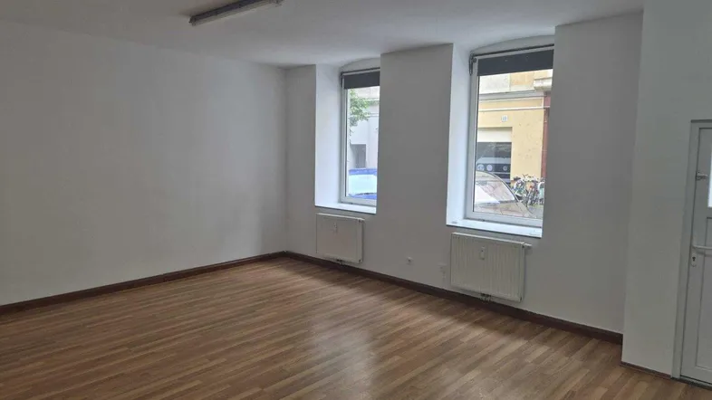 Heller, leerer Raum mit Laminatboden und zwei Fenstern zur Straße, ideal als Bürofläche.