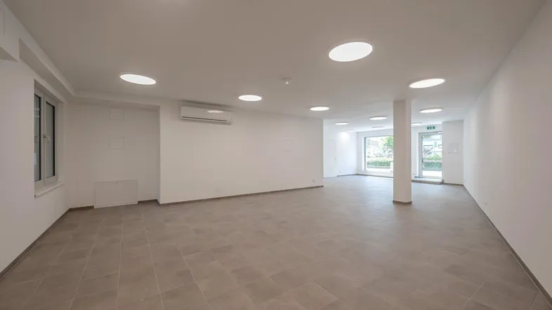 Geräumiger, leerer Raum mit hellen Fliesen, weißen Wänden und integrierter Klimaanlage, ideal für Büro oder Gewerbe.