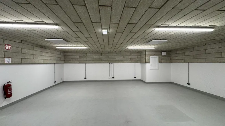 Großer, leerer Lagerraum mit grauem Boden, weißen Wänden und einer strukturierten Decke, gut beleuchtet.