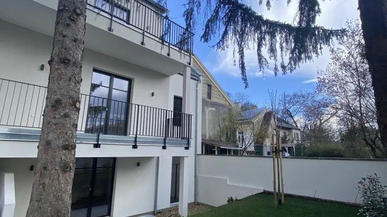 Moderne Wohnanlage mit weißer Fassade, Balkonen und einem gepflegten Rasenbereich im Freien.