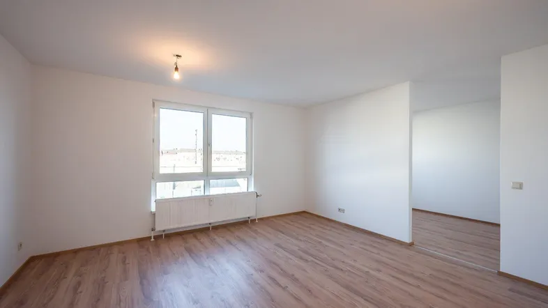 Heller, leerer Raum mit Laminatboden und großem Fenster, bereit zur individuellen Gestaltung.