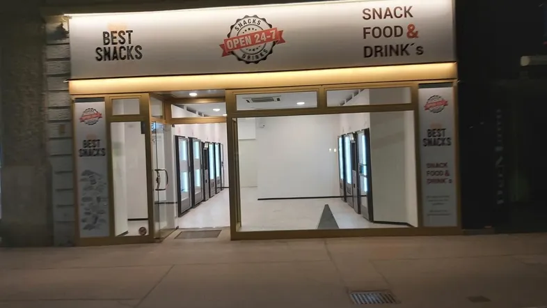 Nachtansicht eines modernen Snack-Shops mit großer Glasfront und Leuchtreklame, der 24 Stunden geöffnet ist.