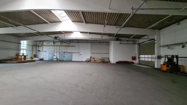 Geräumige, leere Lagerhalle mit hohen Decken, Oberlichtern und Betonboden, bereit zur Nutzung.