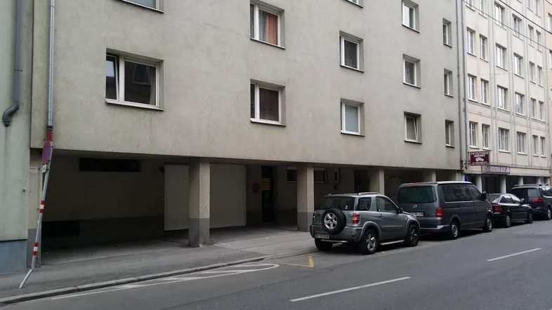 Fassade eines Mehrfamilienhauses mit Parkmöglichkeiten entlang der Straße und überdachtem Eingangsbereich.