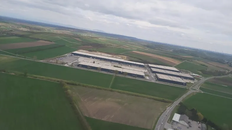 Luftaufnahme von großen Industriegebäuden umgeben von Feldern und Straßen unter bewölktem Himmel.