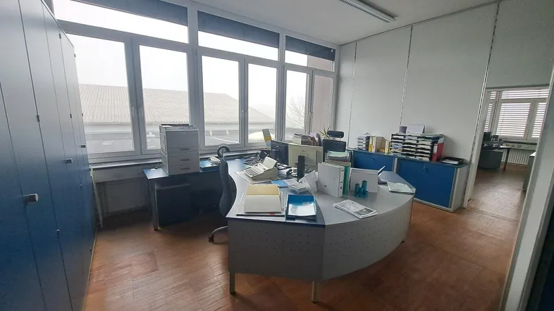 Geräumiges Büro mit großen Fenstern, Holzfußboden und blauen Aktenschränken, das viel Tageslicht bietet.