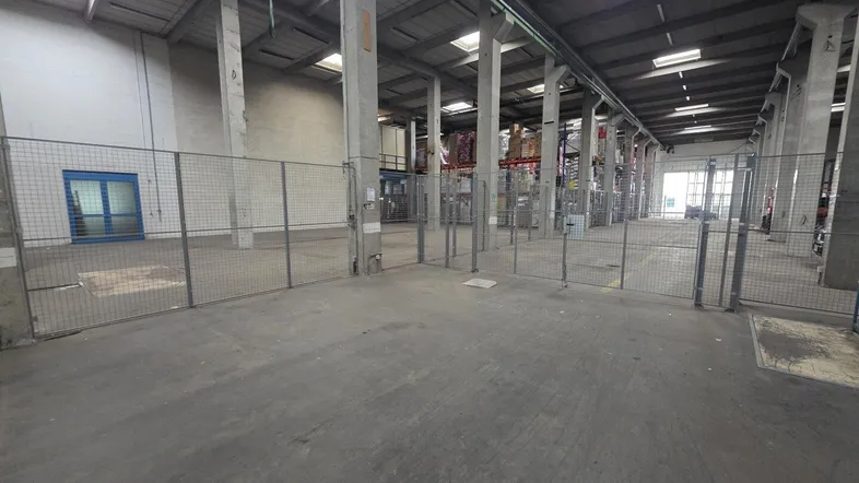 Geräumige Lagerhalle mit Betonboden, hohen Decken und Oberlichtern, durch Gitterzäune unterteilt.