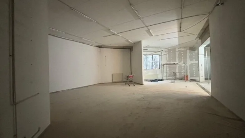Großer, leerer Innenraum in Rohbauzustand mit sichtbaren Installationen und Fenstern, bereit für die Renovierung.