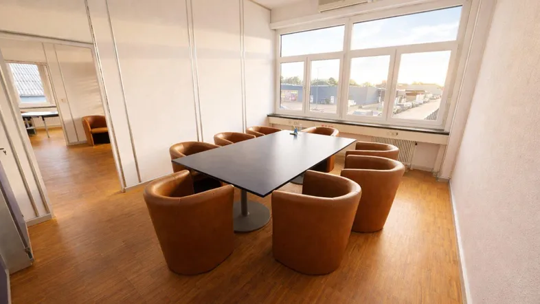 Konferenzraum mit großem Tisch, braunen Stühlen und Blick auf das umliegende Gewerbegebiet.