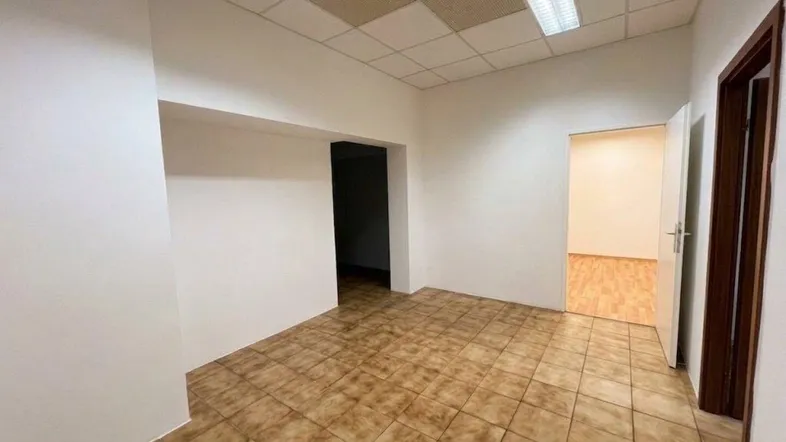 Geräumiger Büroraum mit braunen Fliesen, abgehängter Decke und Zugang zu weiteren Räumen.