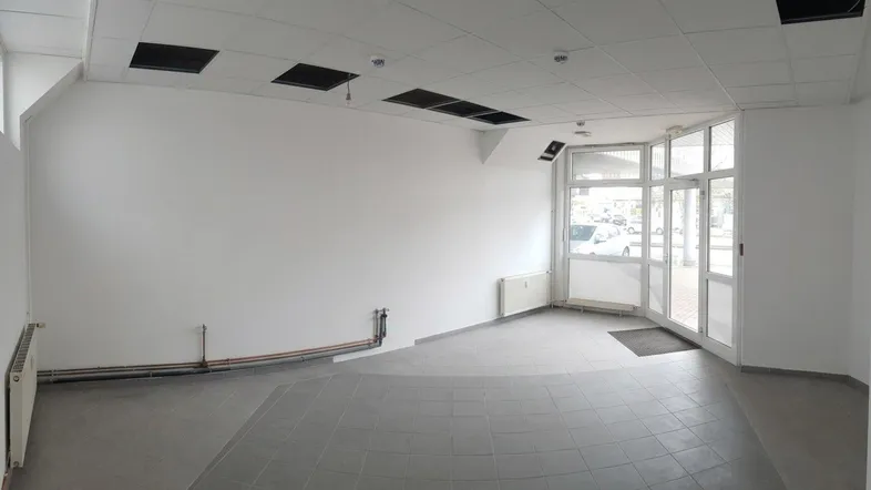 Leerer Gewerberaum mit großen Fenstern, Fliesenboden und abgehängter Decke, bereit zur Gestaltung.