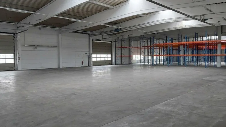 Geräumige Lagerhalle mit hohen Decken, Betonboden und Tageslicht durch Oberlichter und Rolltore.
