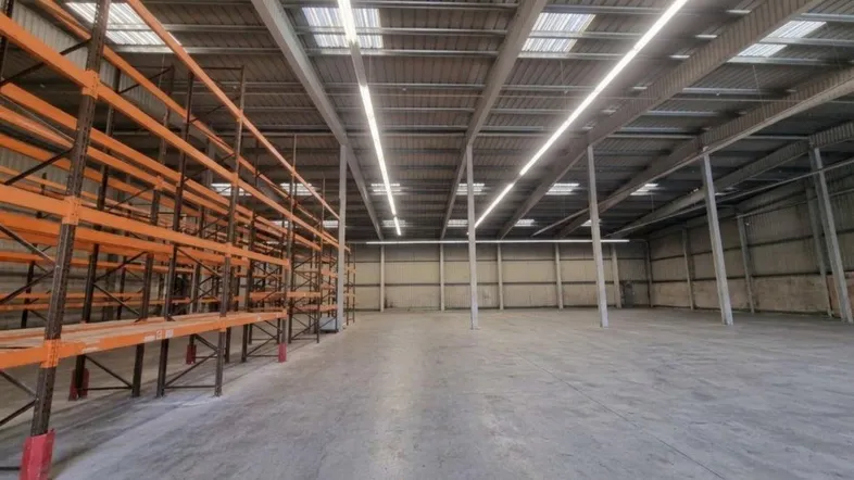 Geräumige Lagerhalle mit hohen Decken, Betonboden, industriellen Regalsystemen und viel Tageslicht durch Oberlichter.