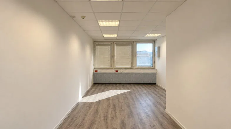 Heller Büroraum mit Laminatboden, weißen Wänden und Fenstern mit Jalousien, bereit zur individuellen Gestaltung.
