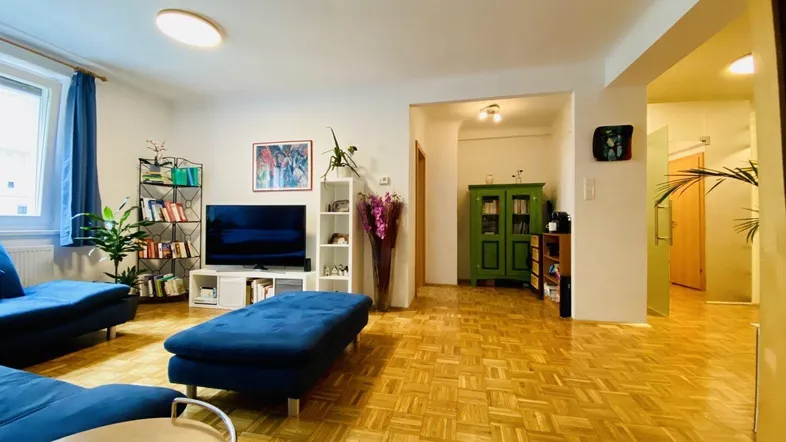 Helles Wohnzimmer mit Parkettboden, blauen Sofas und einem grünen Schrank, der den Raum belebt.