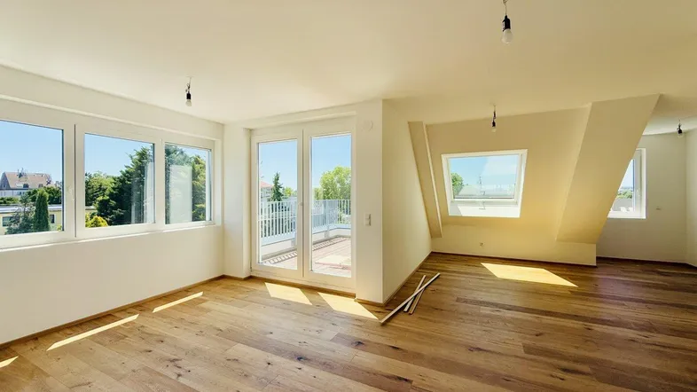 Helles Dachgeschosszimmer mit Holzboden, großen Fenstern und Zugang zu einer Terrasse.