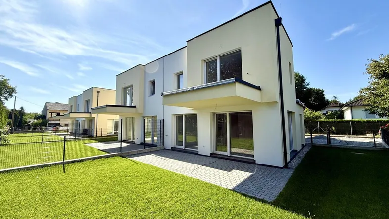 Moderne Doppelhaushälfte mit Garten und Terrasse unter blauem Himmel, ideal für sonnige Tage.