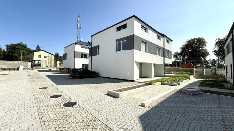 Moderne Reihenhäuser in einer neuen Wohnsiedlung mit gepflasterten Parkplätzen unter blauem Himmel.