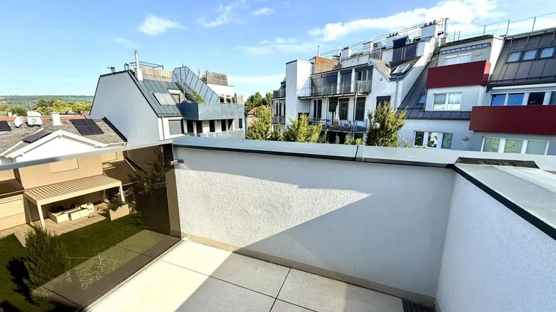 Geräumige Dachterrasse mit Fliesenboden und weitem Blick auf die umliegenden Gebäude und den Himmel.