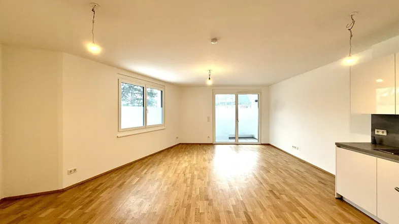 Heller, offener Wohn- und Essbereich mit Parkettboden und Zugang zu einem Balkon.