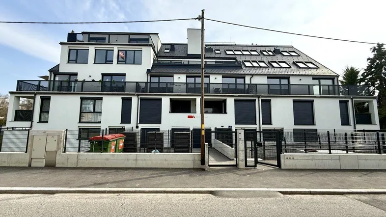 Moderne Wohnanlage mit weißer Fassade, Balkonen und Dachfenstern unter blauem Himmel.