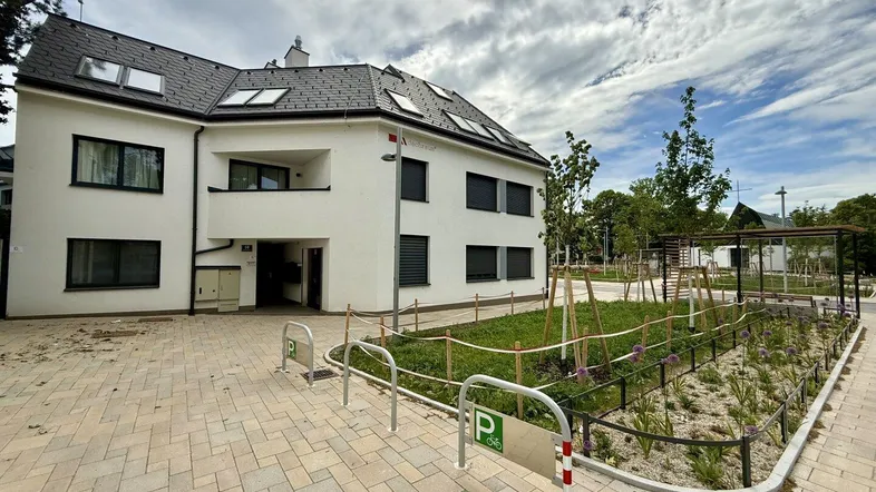 Modernes Mehrfamilienhaus mit weißer Fassade, Satteldach und Außenparkplätzen.