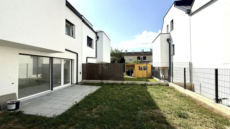 Neuer Gartenbereich mit Rasenfläche und gepflasterter Terrasse hinter modernen Reihenhäusern.