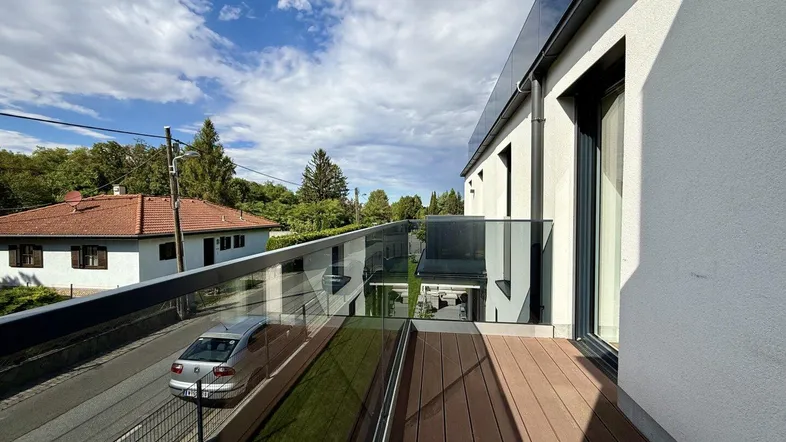 Moderner Balkon mit Glasgeländer und Holzboden, bietet einen Blick auf die Umgebung.