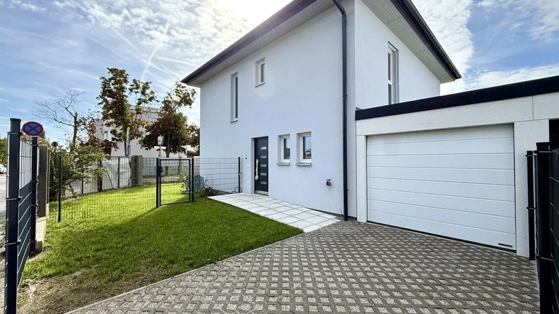 Modernes Einfamilienhaus mit weißer Fassade, Garage und gepflasterter Einfahrt.
