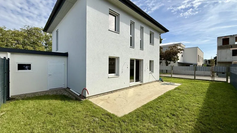 Modernes Einfamilienhaus mit weißer Fassade, Garten und kleiner Terrasse, ideal für sonnige Tage.