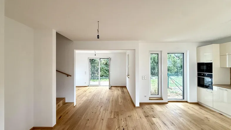 Heller offener Wohnbereich mit moderner Einbauküche, Holzboden und Zugang zum Garten.