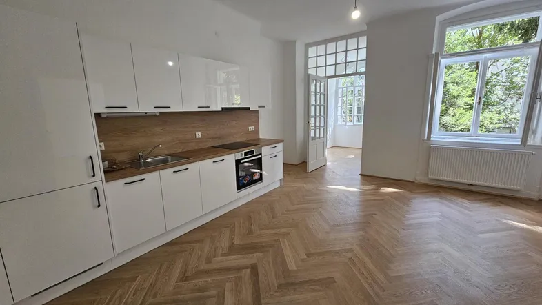 Moderne Einbauküche mit weißen Hochglanzfronten und Fischgrätparkett in einem hellen Raum.