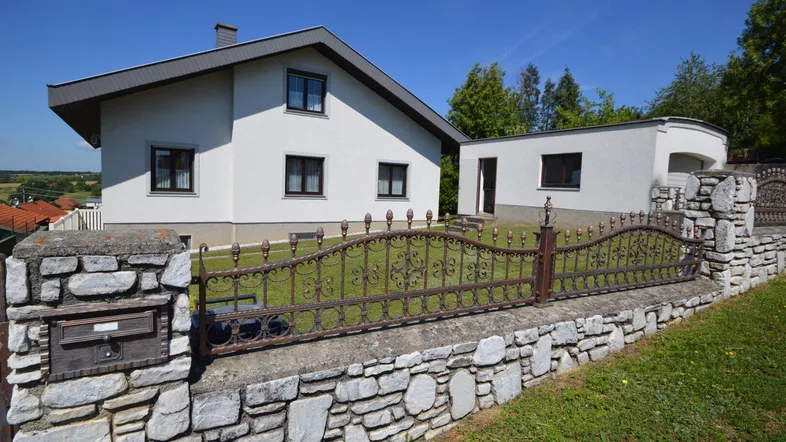 Weißes Einfamilienhaus mit Steinfassade, schmiedeeisernem Zaun und gepflegtem Vorgarten.