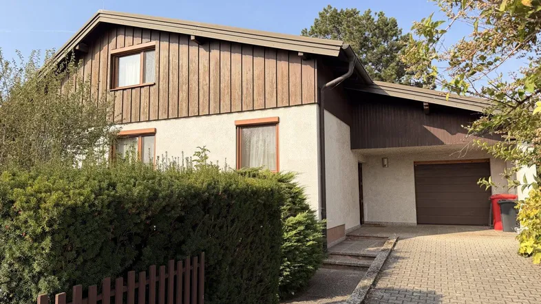 Einfamilienhaus mit Holzverkleidung, heller Fassade und gepflasterter Einfahrt zur Garage.