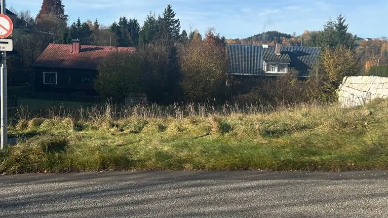 Unbebautes Grundstück mit Blick auf umliegende Häuser und Bäume unter blauem Himmel.