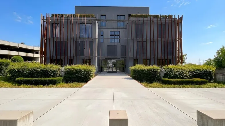 Modernes Bürogebäude mit einzigartiger Fassadenverkleidung und gepflegter Grünanlage unter blauem Himmel.