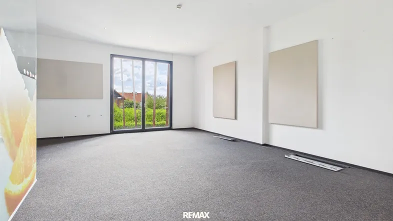 Geräumiger, heller Büroraum mit Teppichboden und großen Fenstern, die einen Blick ins Grüne bieten.