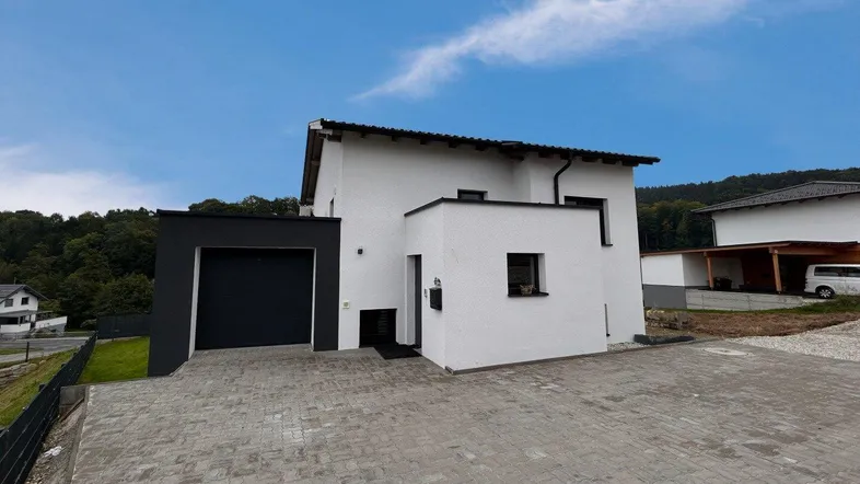 Modernes Einfamilienhaus mit weißer Fassade, integrierter Garage und gepflasterter Zufahrt.
