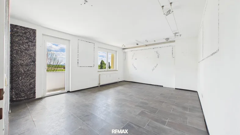 Heller, leerer Raum mit grauen Fliesen, weißen Wänden und Zugang zu einem Balkon.