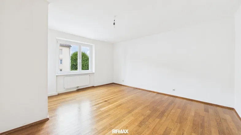 Helles, leeres Zimmer mit Parkettboden und einem Fenster, das einen Blick ins Grüne bietet.