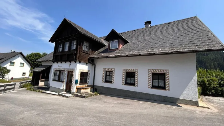 Traditionelles Haus mit dunklem Satteldach und weißer Fassade unter blauem Himmel.