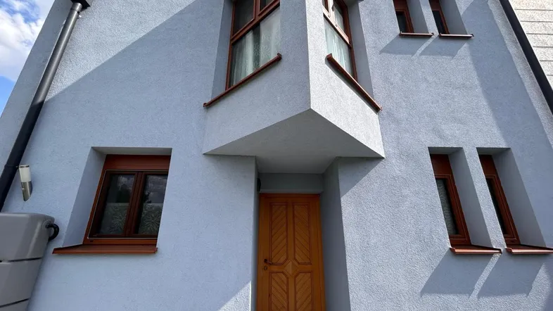 Fassade eines modernen Hauses mit hellblauer Putzfassade und braunen Fenstern.